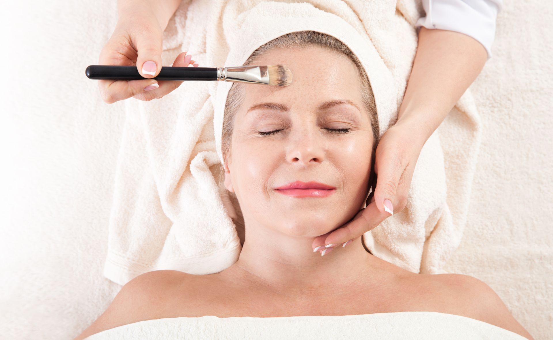 Facial spa treatment with brush applied to forehead while client lies relaxed on a towel