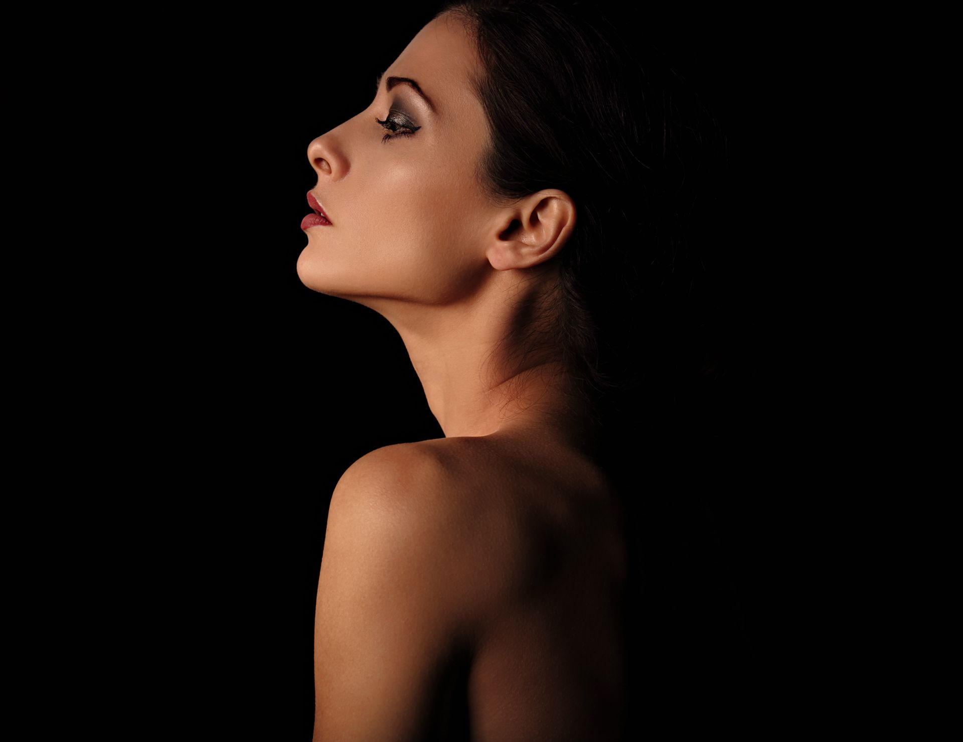 A woman without a shirt is looking over her shoulder in the dark.