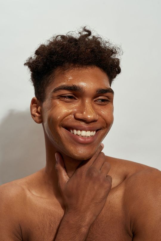 A shirtless young man is smiling while washing his face.