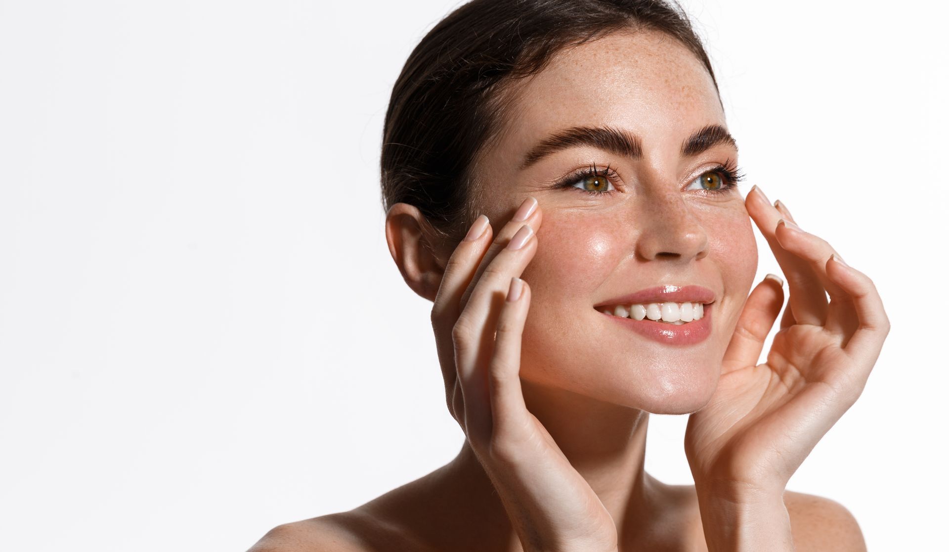 A woman is touching her face with her hands and smiling.