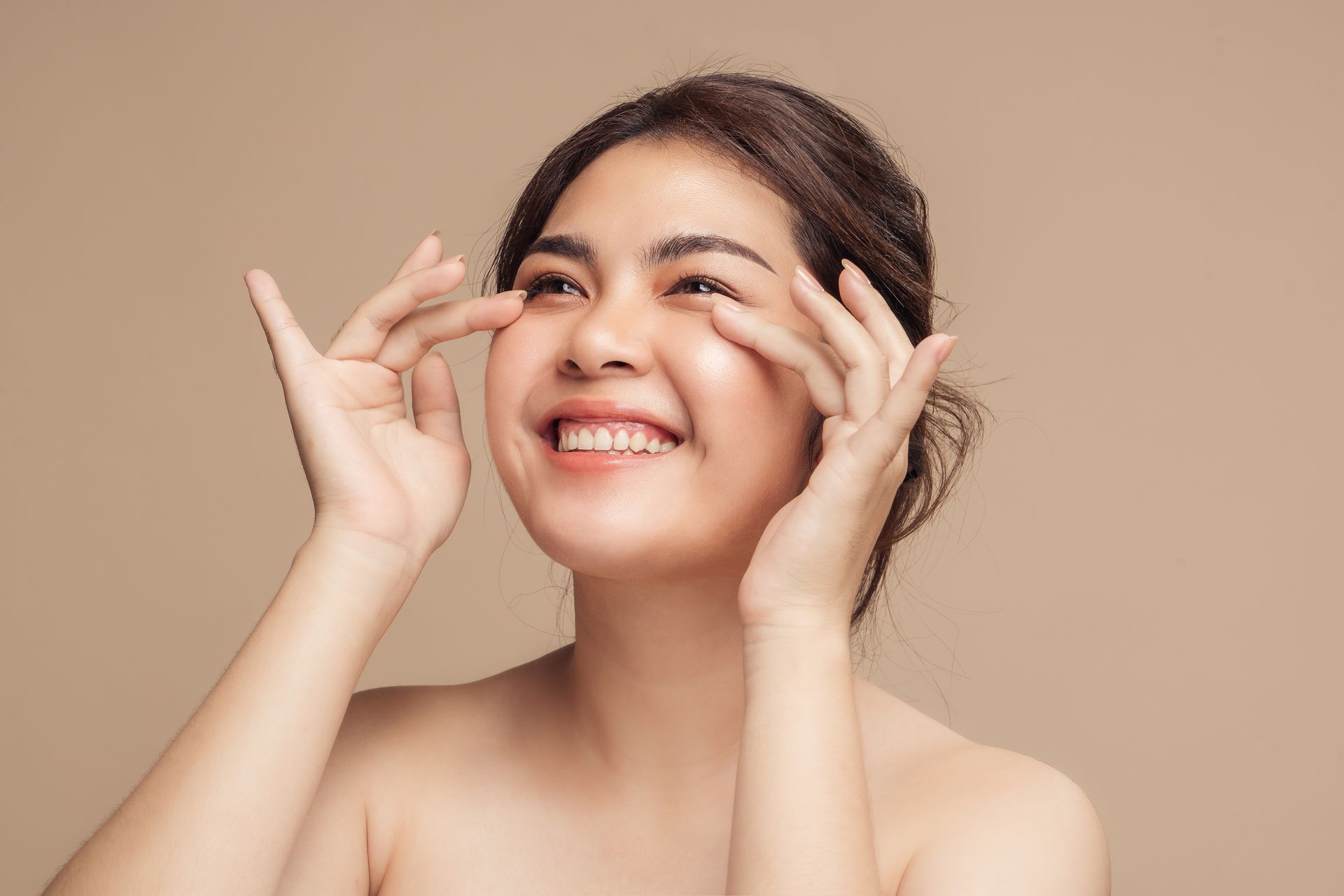 A woman is smiling and touching her face with her hands.