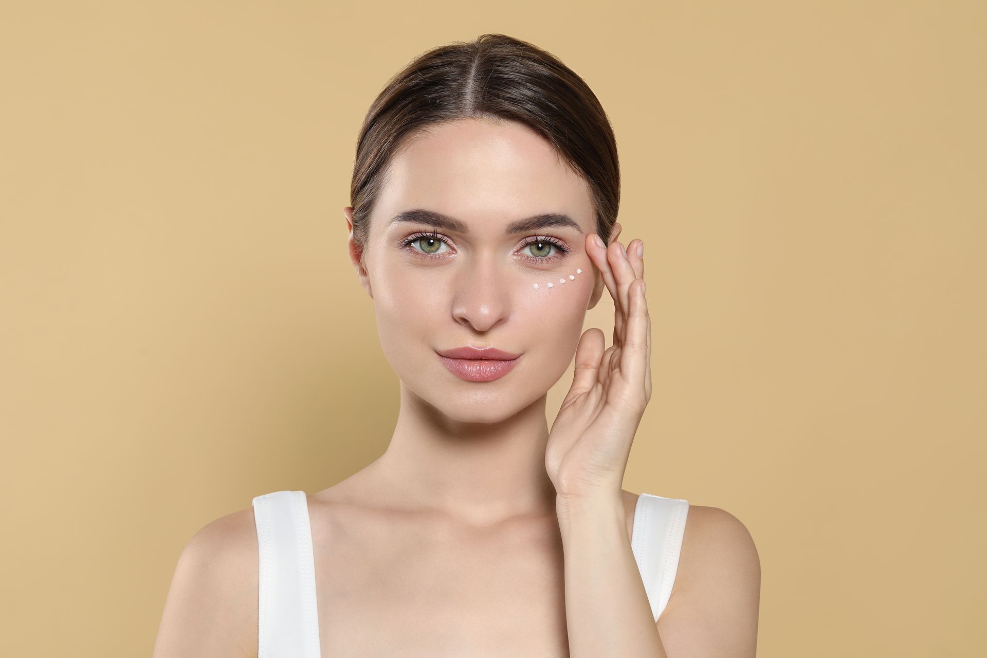 A woman is applying eye cream to her face.