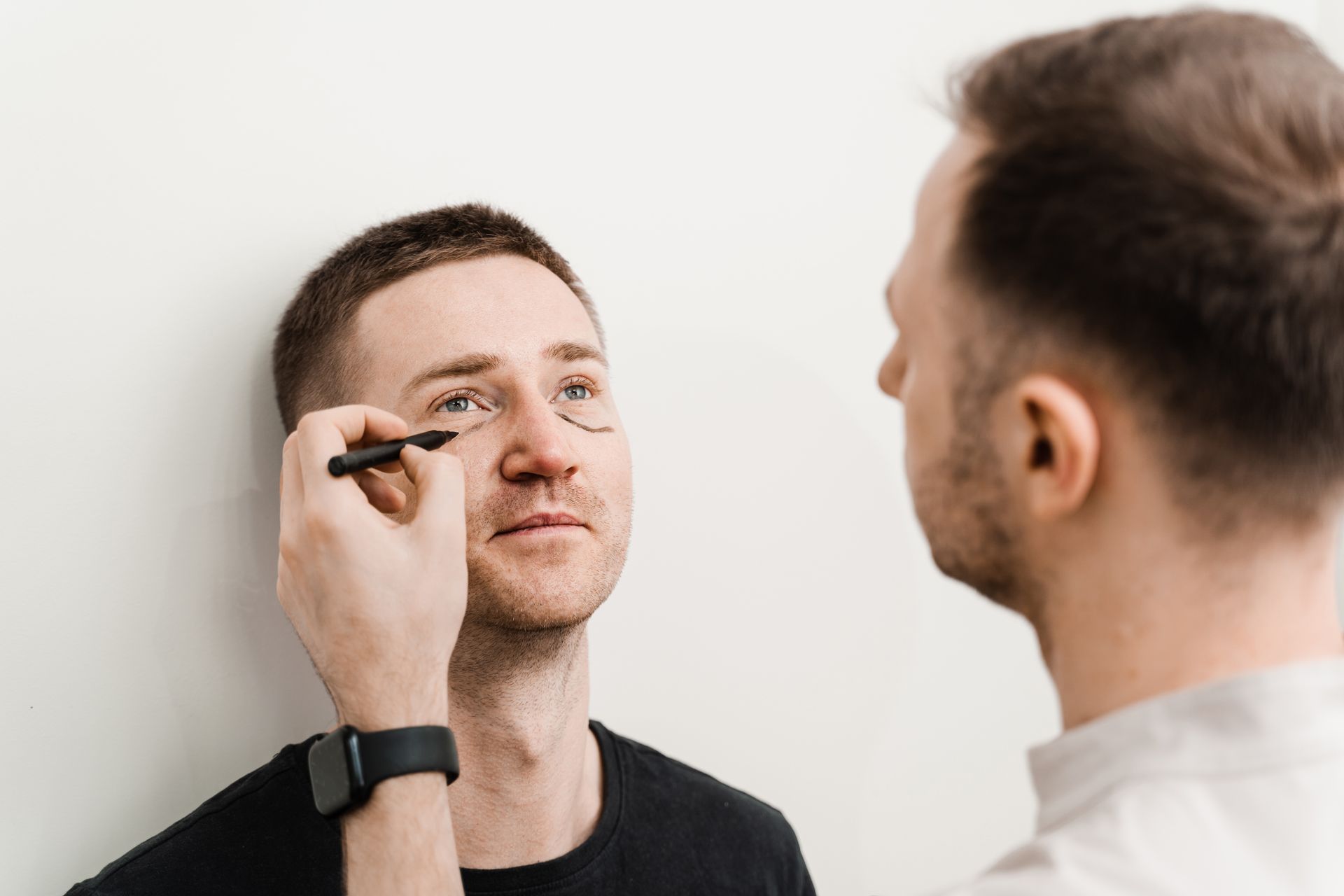 A man is applying eyeliner to another man 's eye.