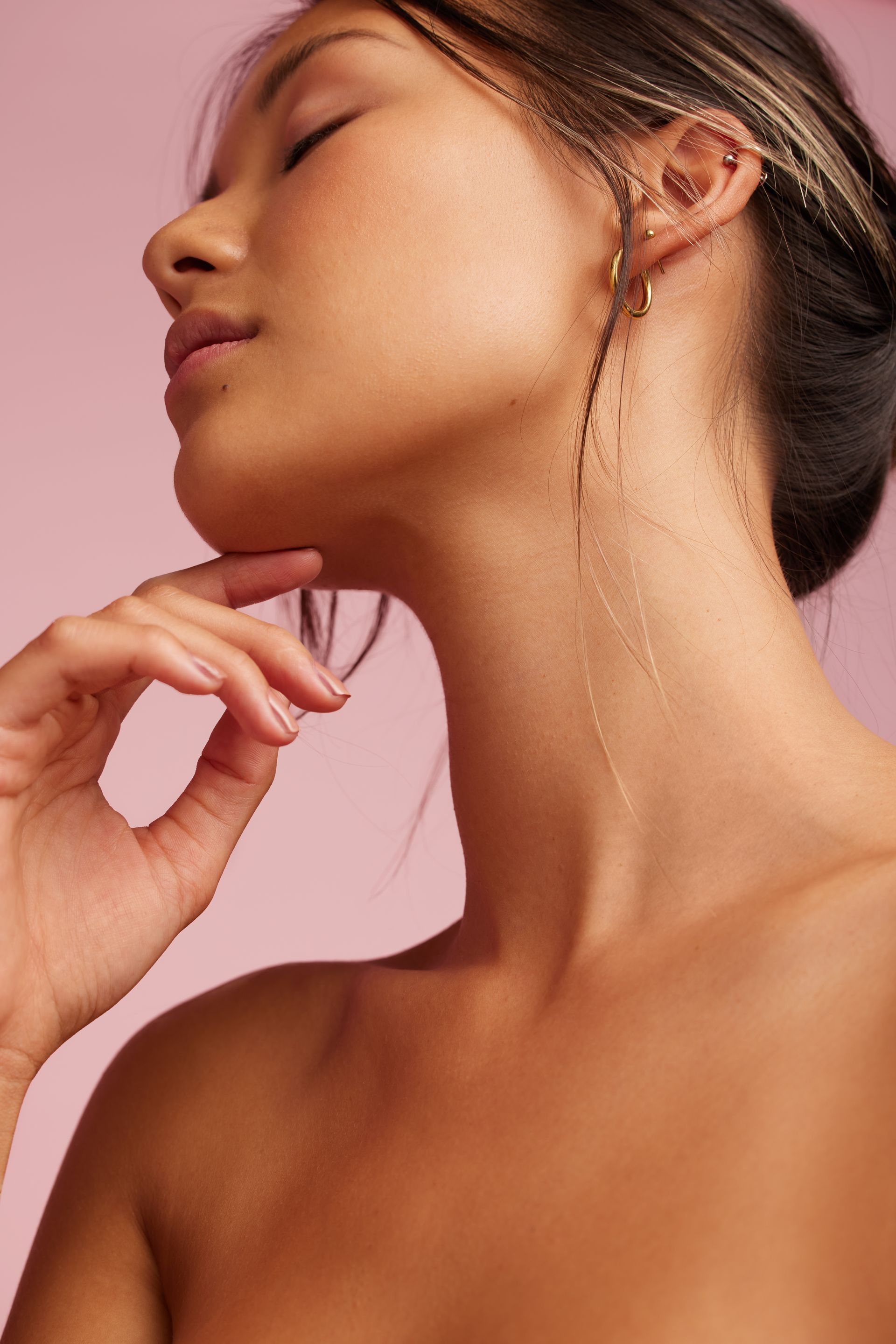 A woman is touching her neck with her hand while wearing earrings.