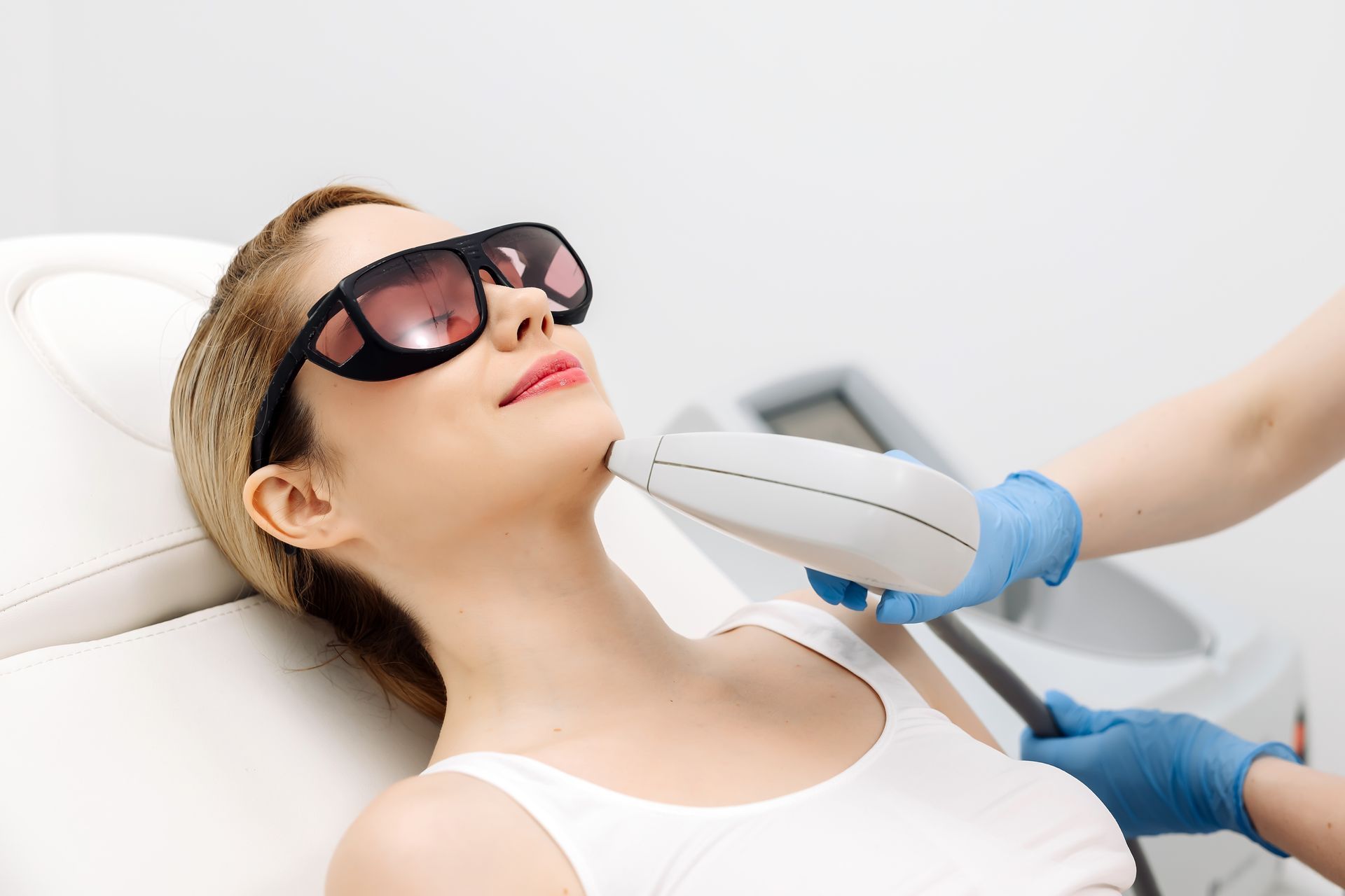 A woman wearing sunglasses is getting a laser hair removal treatment on her face.