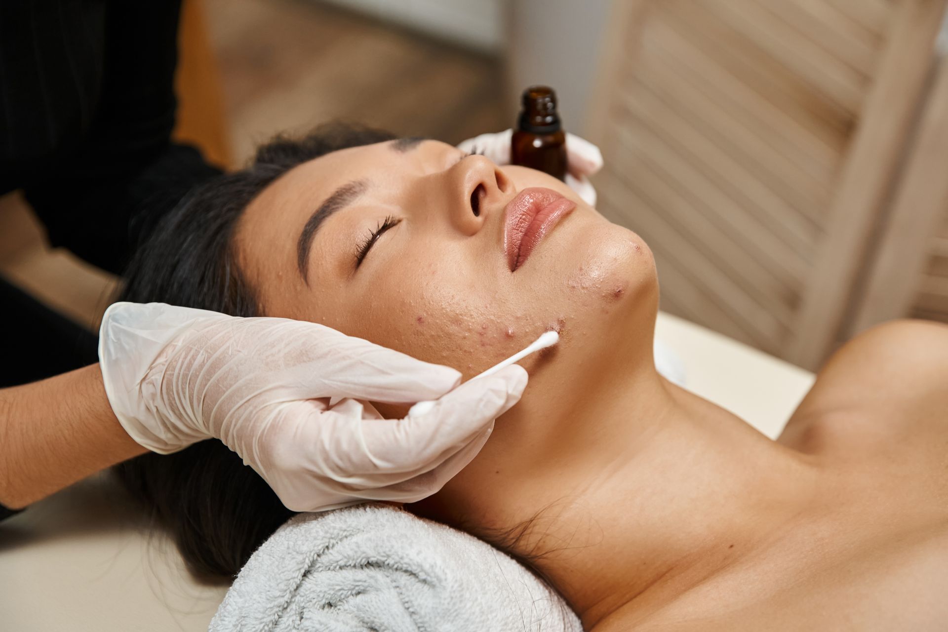 Woman receiving a facial treatment, where a gloved hand applies product to her face with a cotton swab.
