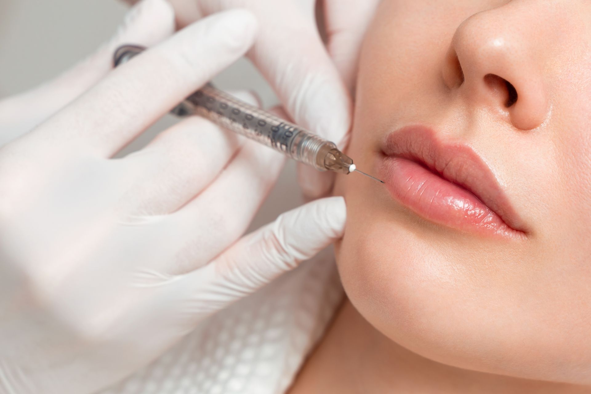 Gloved hand using a syringe near a woman's lips during a cosmetic procedure