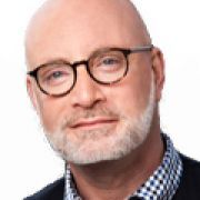 A bald man with a beard and glasses is looking at the camera.