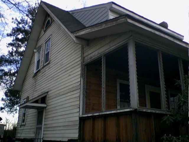 Old, weathered two-story house with porch, light siding, and dark roof.