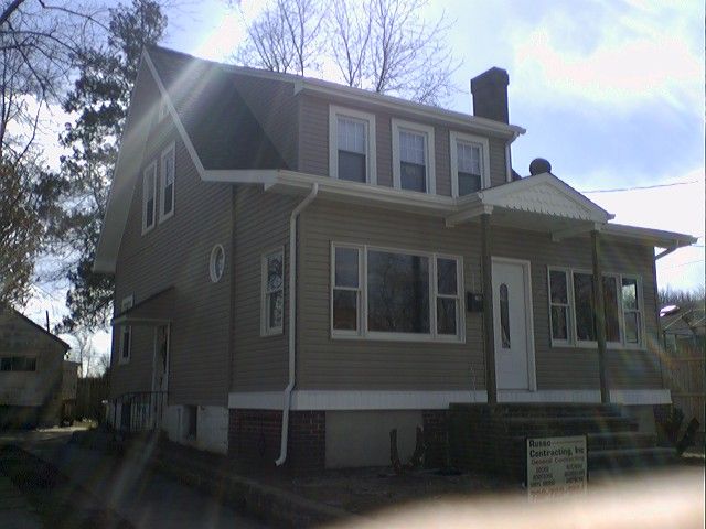 Beige two-story house with white trim and a porch under a sunny sky.