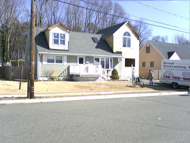 House under construction, light green siding, with a gray roof, and two people near a white van.