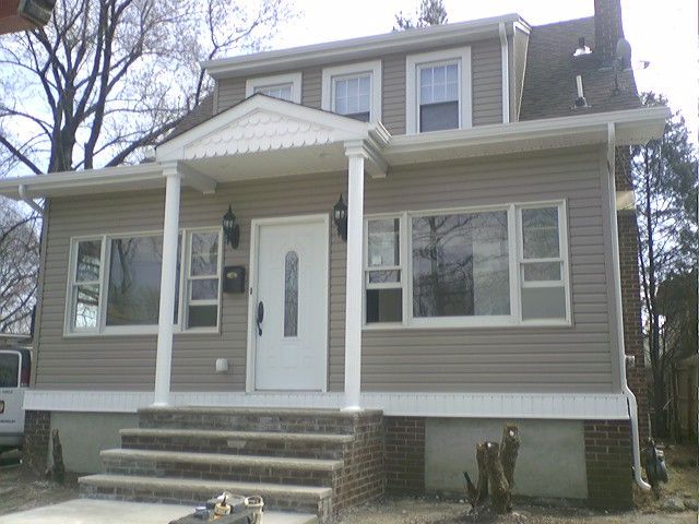 Tan two-story house with a white porch, columns, and brick foundation.