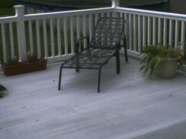 A black lounge chair on a white deck, with a white railing and potted plants.