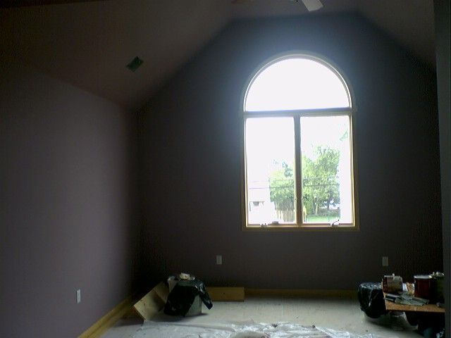 Room with tall arched window; purple walls, tan trim, and construction materials on the floor.