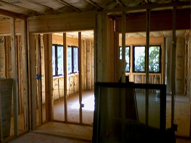 Interior of a building under construction, wooden frame walls, windows, insulation, natural light.