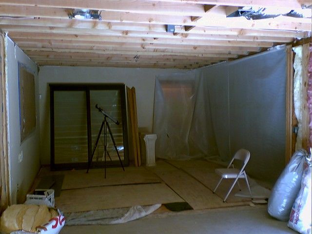 Basement under construction; exposed wood framing, plastic sheeting on walls, sliding glass door, and insulation.