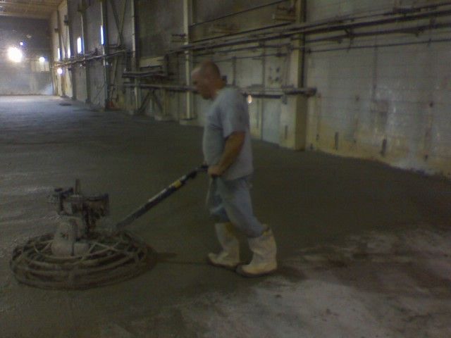 Man using a concrete finishing machine in a large, industrial space.