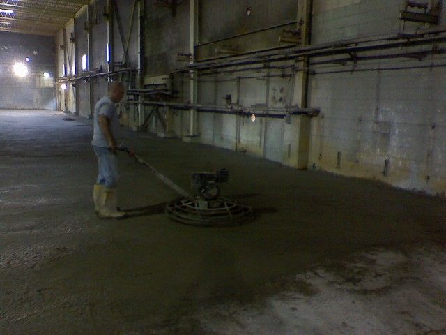 Man smoothing wet concrete floor with power trowel in industrial setting.