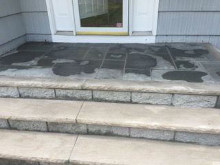 Gray concrete porch and steps, wet, with a white door and siding above.