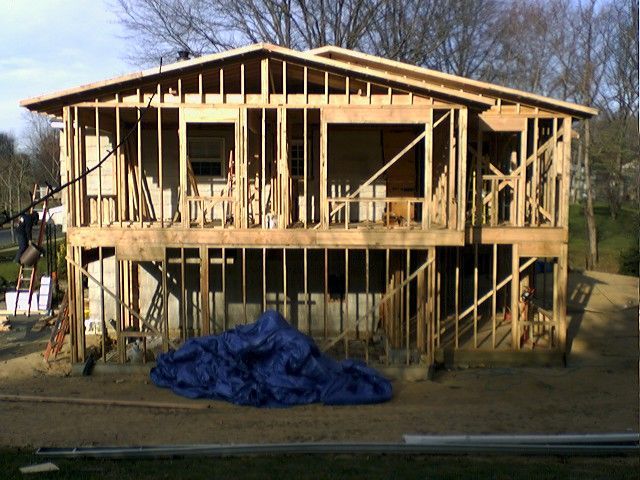 Two-story house under construction; wooden frame visible, with a blue tarp in the foreground.