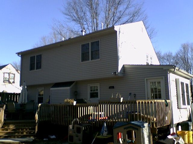 Back of a two-story house with a wooden deck. Beige siding, windows, door, and a clear sky.