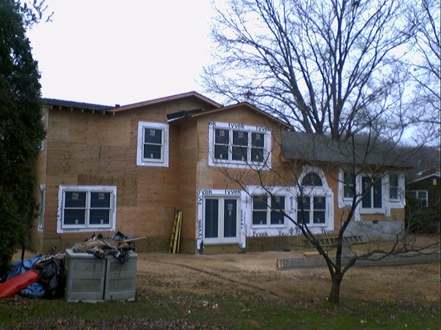 Two-story house under construction, wooden frame, windows installed, overcast sky, outdoor setting.