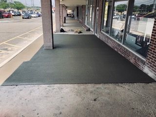 A concrete sidewalk under a building's overhang, freshly poured in gray, with brick facade on right.