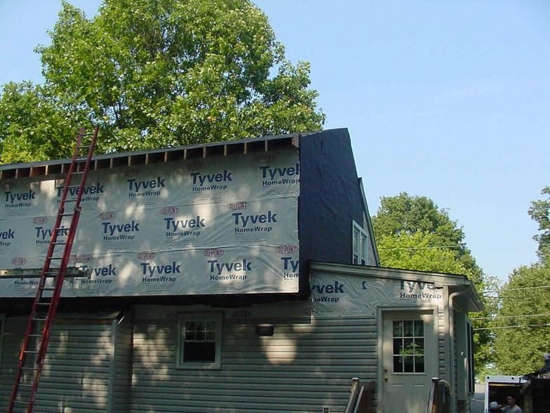 House under construction, covered in Tyvek. Ladder leans against the structure.