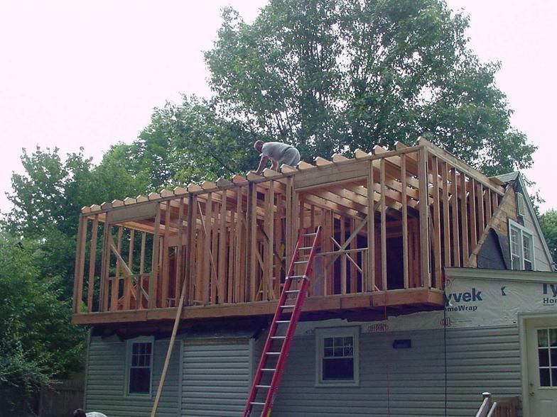 Construction of a second-story addition on a house; a worker on the wooden frame with a red ladder.