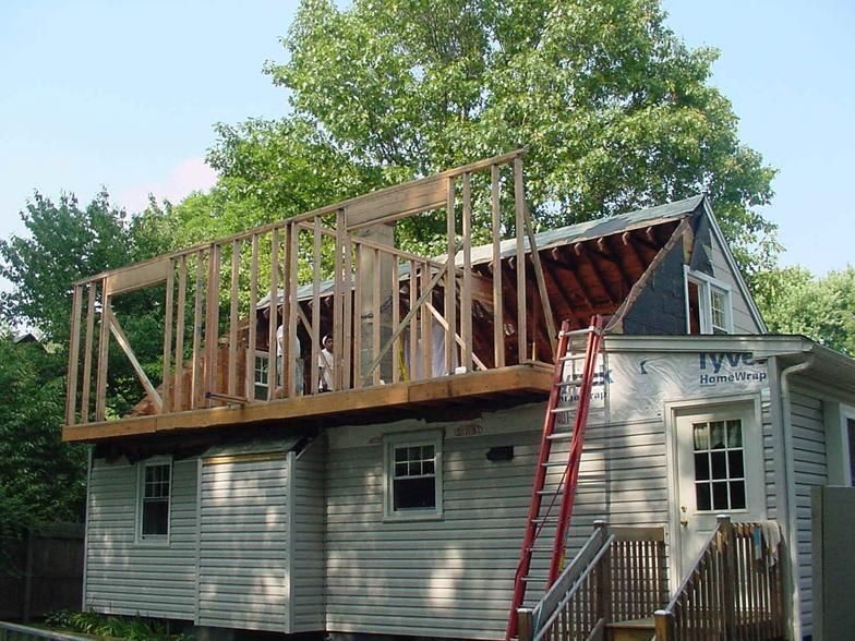 Construction of a wooden deck and wall framing on a two-story house. A red ladder leans against the house.