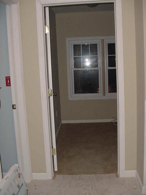 Doorway into a room with window. Beige walls, white trim, brown carpet, and light streaming through the window.