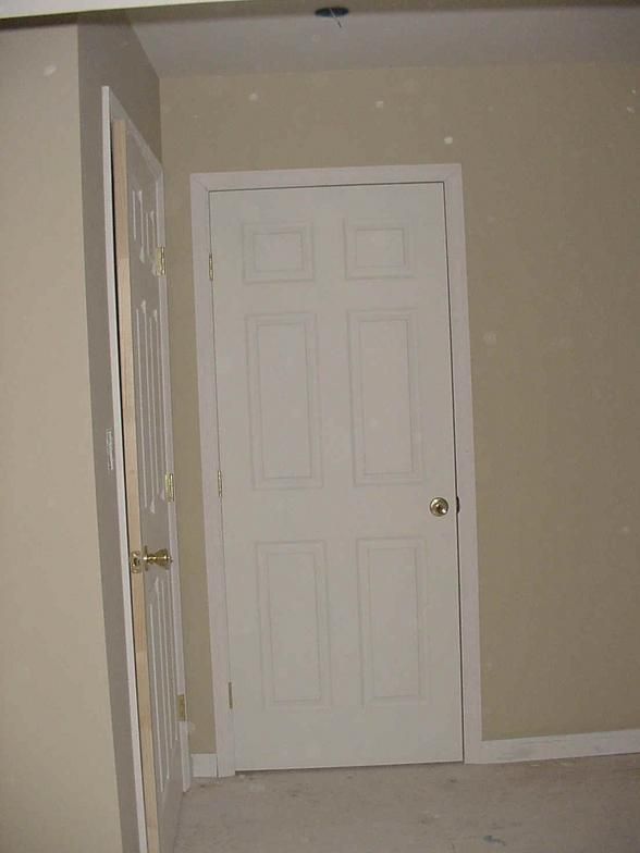 White door in a room with beige walls and another open door to the left.