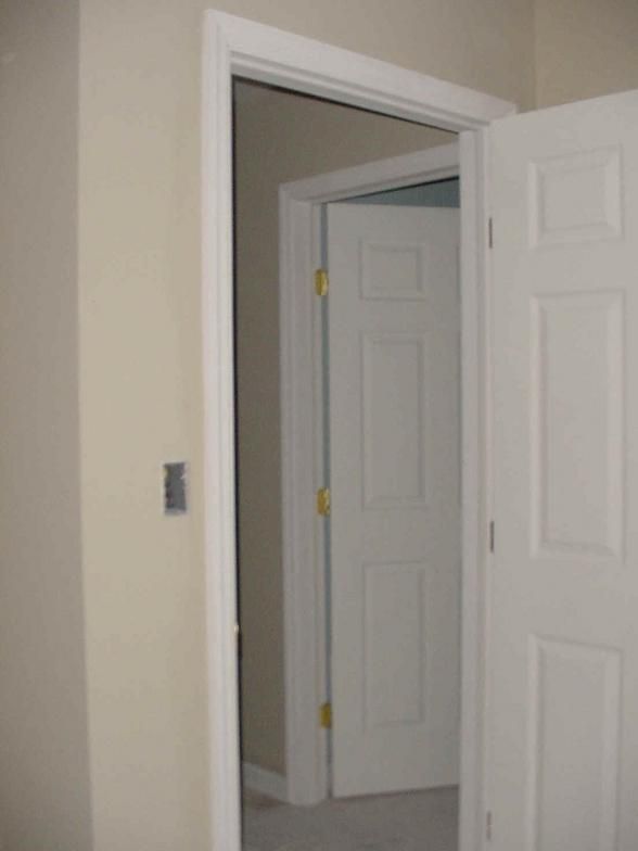 White door ajar, revealing another white door and doorway, light beige walls.