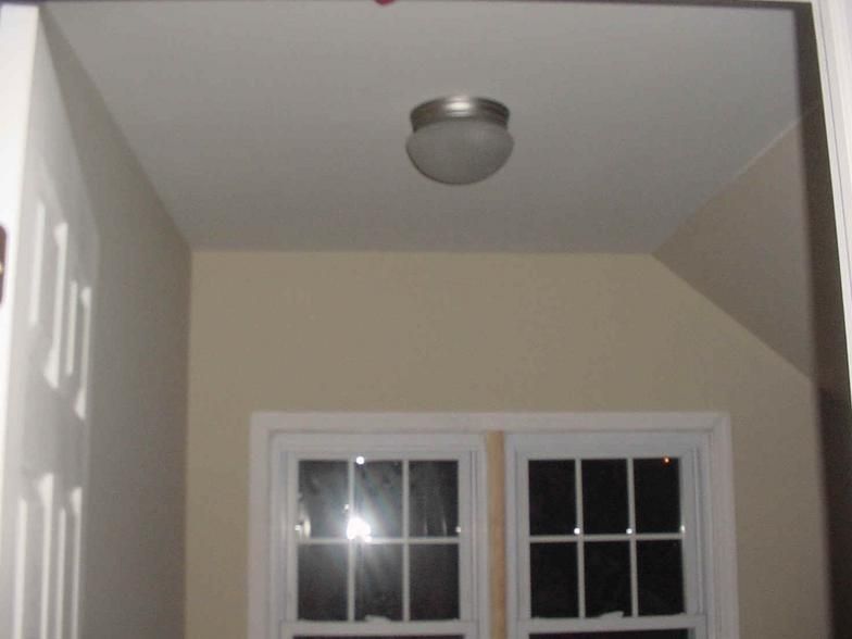 Interior view: A ceiling-mounted light fixture hangs above two windows, a doorway to the left.