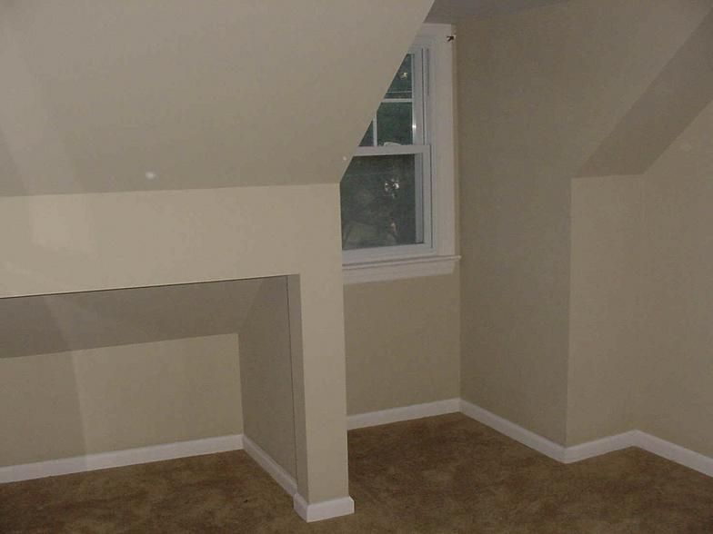 Empty attic room with beige walls, carpet, a window, and angled ceiling.