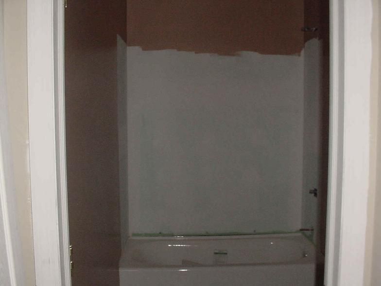 Bathroom with white tub, gray shower surround, and brown walls.