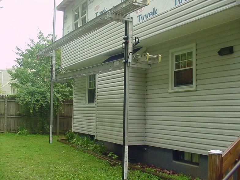 House with siding repair in progress, using a scaffolding-like structure; outdoors, daylight.