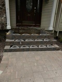 Brown steps made of blocks lead to a brown door. Beige siding and paving stones are visible.