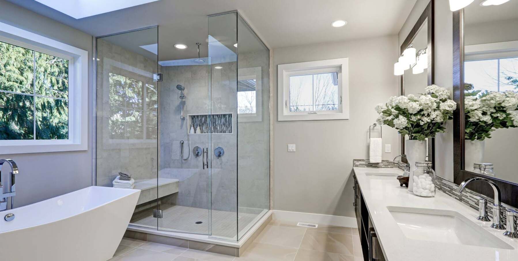 A modern bathroom with a glass shower, a bathtub, and a double sink vanity with white flowers.