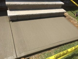 Freshly poured concrete pathway and landing leading to stone steps. Yellow caution tape borders the grass.