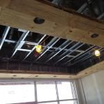 View of a construction site ceiling with exposed metal framing, wooden beams, and lights.