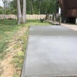 Newly poured concrete patio next to a grassy lawn. House with a dark-brown roof on the right.