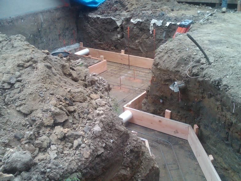 Excavation site with wooden forms, concrete reinforcement, and soil piles.