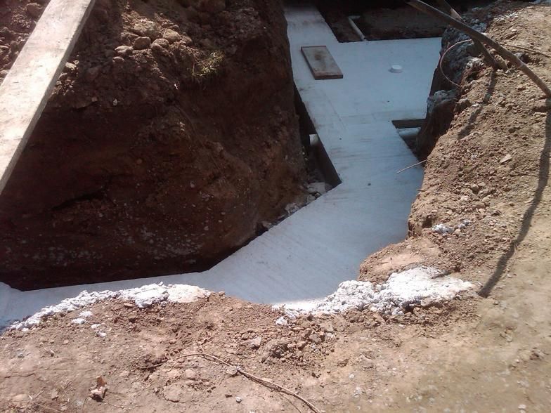 A narrow trench with freshly poured concrete foundation, surrounded by brown soil.