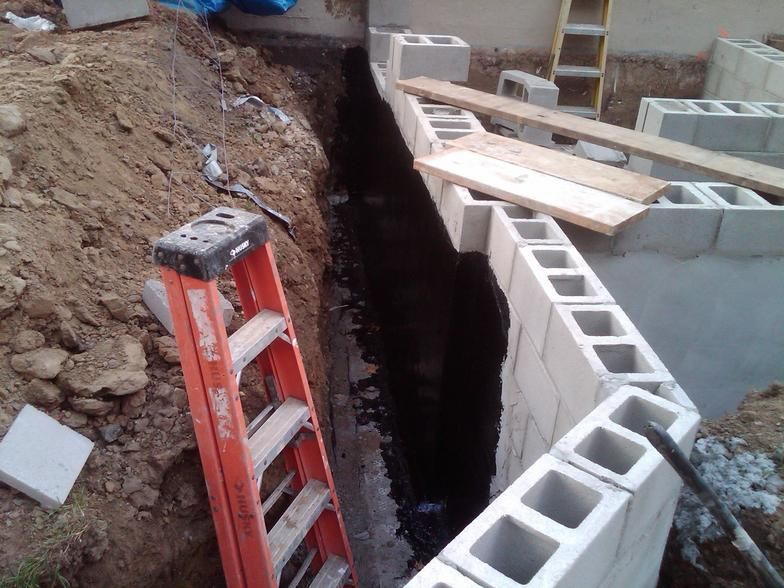 Construction site: Trench next to concrete block wall, with orange ladder in the foreground.