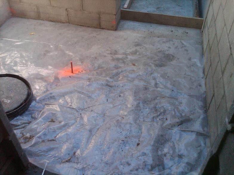 Concrete floor covered with clear plastic sheeting inside a room with cinder block walls; construction site.