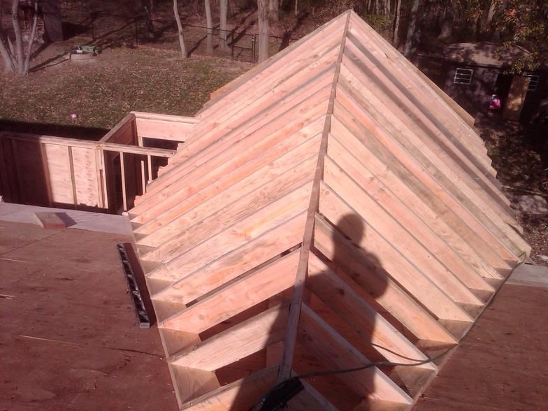 Wooden roof frame under construction, seen from above, with a person's shadow.