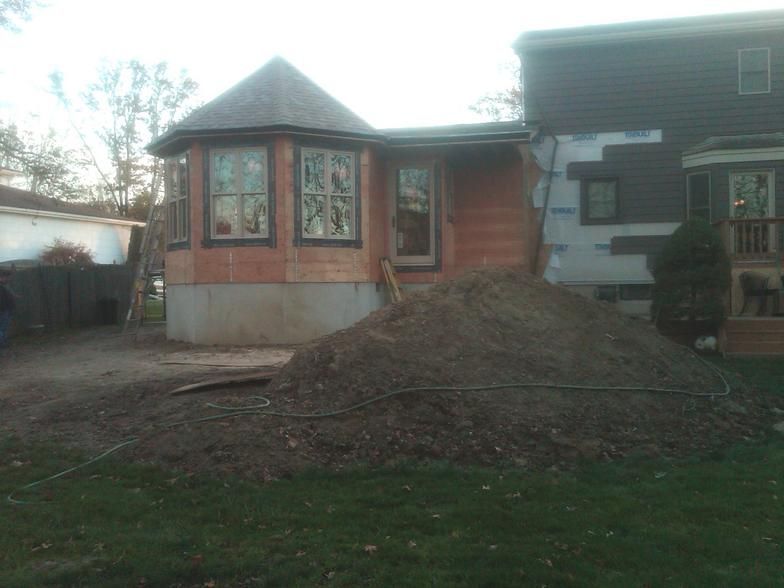 Exterior of a house under construction with a large pile of dirt and a bay window.