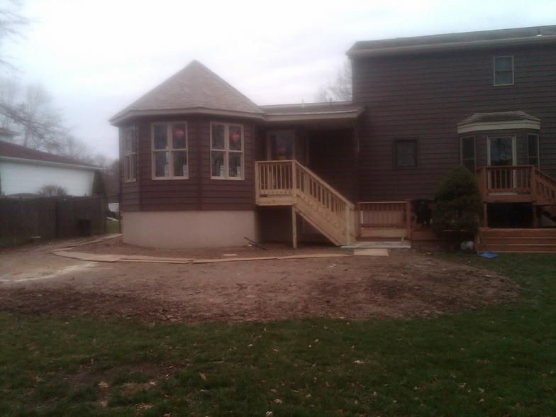 Backyard view of a house with a wooden deck and sunroom. Brown siding and a grassy yard.