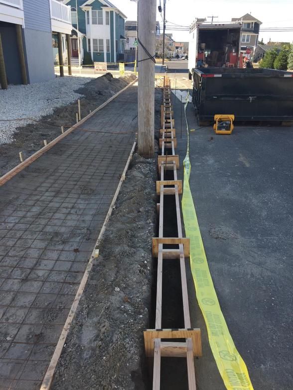 Construction site: forms set for concrete sidewalk and curb. Rebar in sidewalk, yellow caution tape.